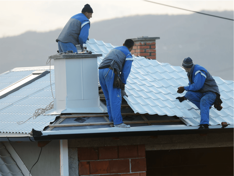 3 men working on metal roof near chimney