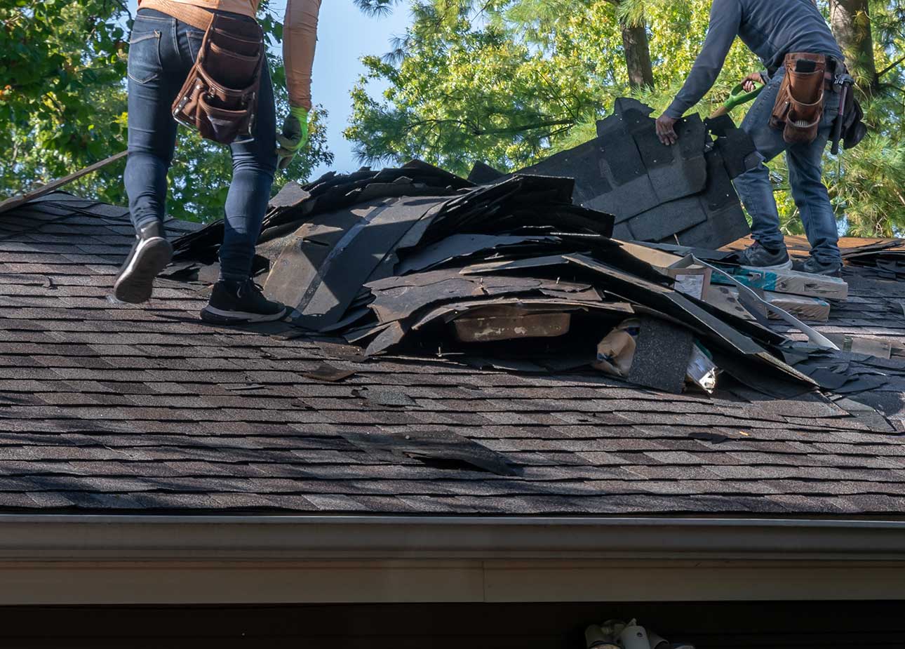 Roofers removing old roof shingles from a house in preparation for storm damage repair.