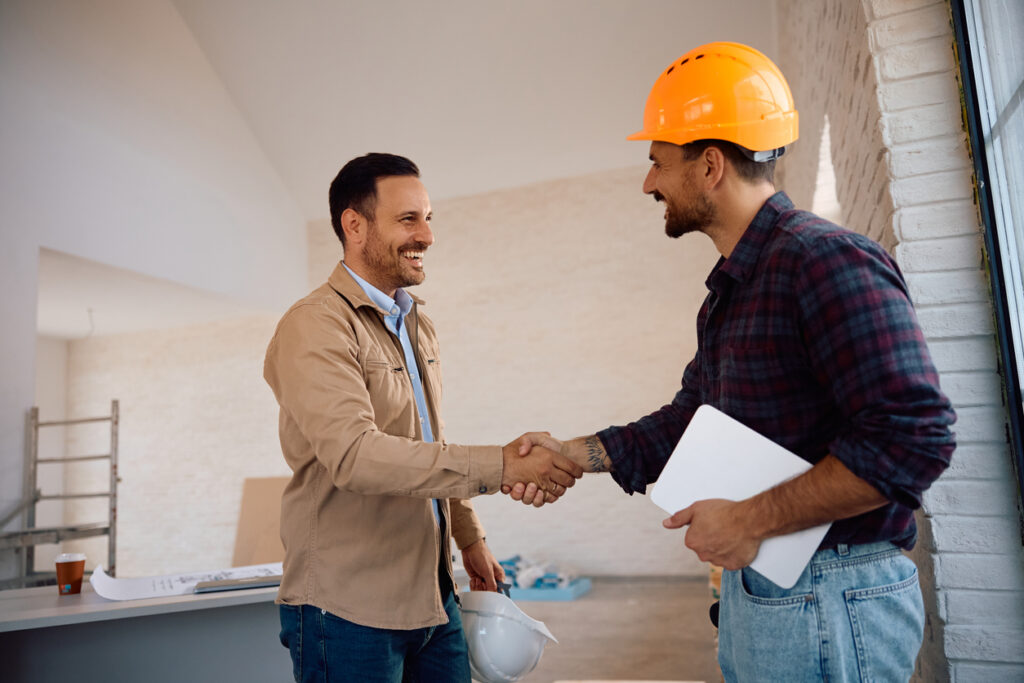 Happy worker and his clients shaking hands at construction site.